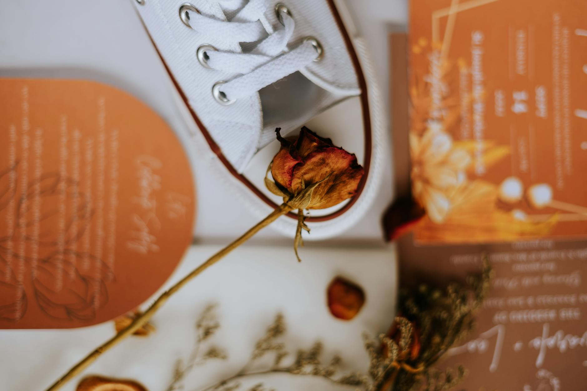 Białe buty ślubne, sucha róża i minimalistyczne zaproszenia na tle