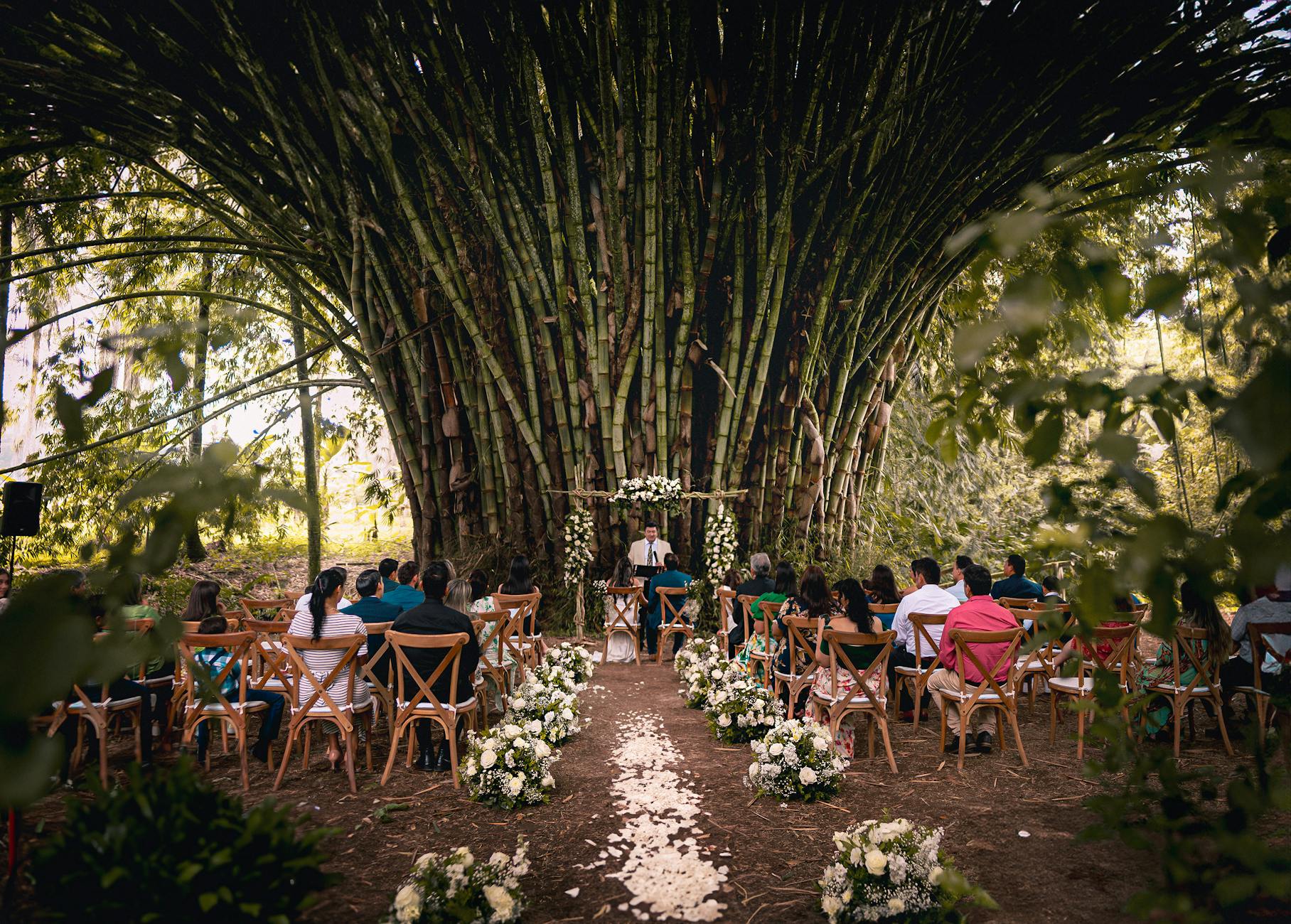 Plenerowy ślub w lesie z eleganckimi kwiatami i gośćmi na krzesłach
