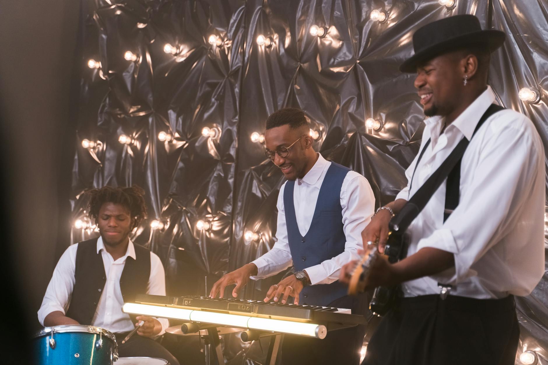 Trio muzyków weselnych grających na scenie z perkusją, klawiszami i gitarą